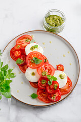 Classic italian salad caprese served in original form with different tomatoes, mozarella, pesto sauce and basil
