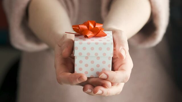 Giving Gift for Special Day as Valentines Day, Mother's Day Father's Day. Unrecognizable Person Holding Present Box with Red Ribbon Towards to Camera. Indoor Daylight Slow Motion Shot. 4K Prores 422