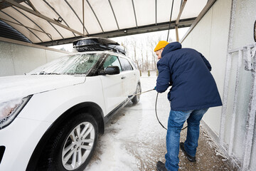 Man washing high pressure water american SUV car with roof rack at self service wash in cold weather.