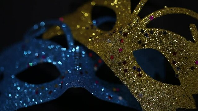 Two luxury traditional venetian masks on dark background illuminated and sparkles from the darkness. Blue and gold shiny carnival masquerade fantasy mask with small colorful stars under light in dark