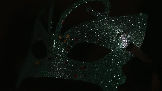 Luxury traditional venetian mask on dark background sometimes illuminated and sparkles from the darkness. Blue shiny carnival masquerade fantasy mask with small colorful stars under light in dark