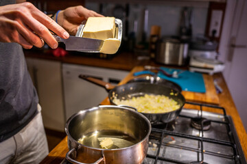 A boy putting butter in a cooking pot.
