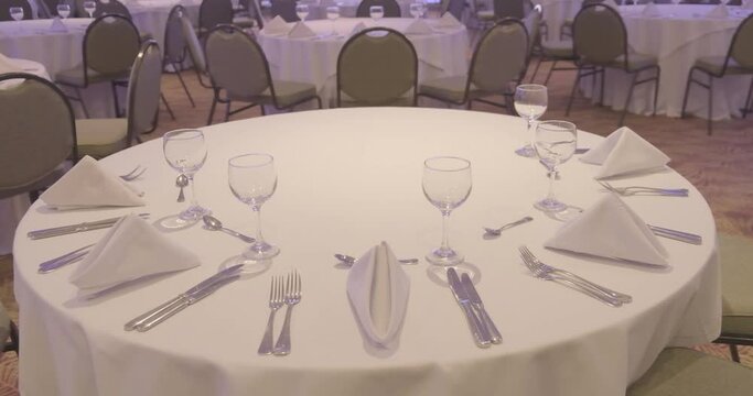 Mesa decorada para evento corporativo con mantel de color blanco, cubiertos y copas de cristal vacias