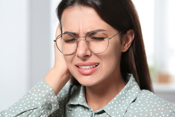 Young woman in eyeglasses suffering from ear pain indoors, closeup