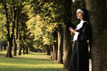 Young nun reading Bible in park on sunny day, space for text