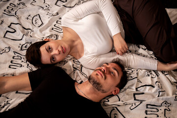 Beautiful couple are lying on the bed and looking at the camera. Young couple photographed from above. - 565448917