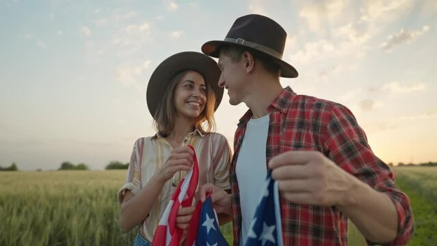 4k slow motion of happy patriotic couple celebrating fourth of july with national flag in rural lardmark at sunset. Federal holiday. 4 July Independence day celebrating with national American flag