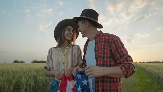 4k slow motion of happy patriotic couple celebrating fourth of july with national flag in rural lardmark at sunset. Federal holiday. 4 July Independence day celebrating with national American flag
