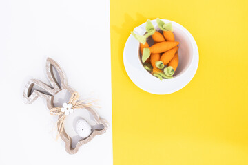 Top view aerial image of decoration and simbol of Easter holidays. Bunny and carrotts in white cup.White and yellow backgrounds with copy space.