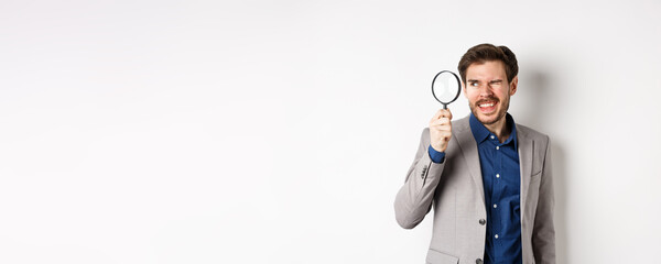 Funny guy in suit investigating or searching for something, looking through magnifying glass,...