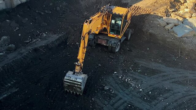 Long shot: the yellow excavator digs black ground with a bucket
