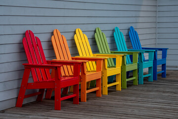Colorful beach chairs outdoors on a wooden deck in a line of rainbow colors 