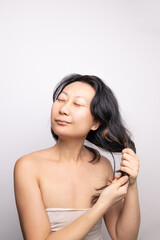 Smiling young Asian woman applying hair mask in a bathroom; haircare concept.