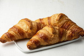 Top view of three croissants on white plate and white background, horizontal, with copy space