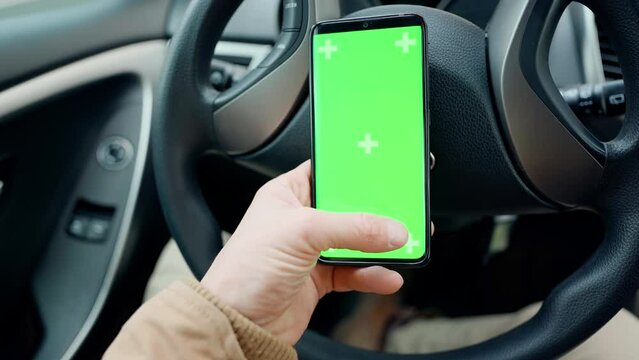 POV man in car at driver place, holds a phone with green screen with marks in hand. driver holds phone against steering wheel, swiping by finger in different directions. navigation, shopping concept