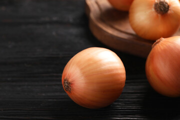 Ripe onions on black wooden table, closeup