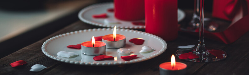 Obraz na płótnie Canvas Saint Valentine's Day celebration. Red burning candles, hearts, gift box, postcard on dark wooden background. Happy holiday. Table decor for festive dinner, romantic atmosphere. Banner