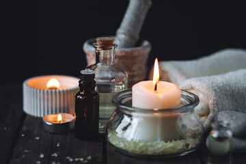 Spa setting with essential oil, candle, sea salt, pebbles, towel on dark wooden background. Massage, aromatherapy. Natural organic ingredients for relaxation, detention. Wellness in salon concept