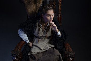 An authoritative, self-confident woman in a Viking-style fantasy costume, sitting on a high chair...