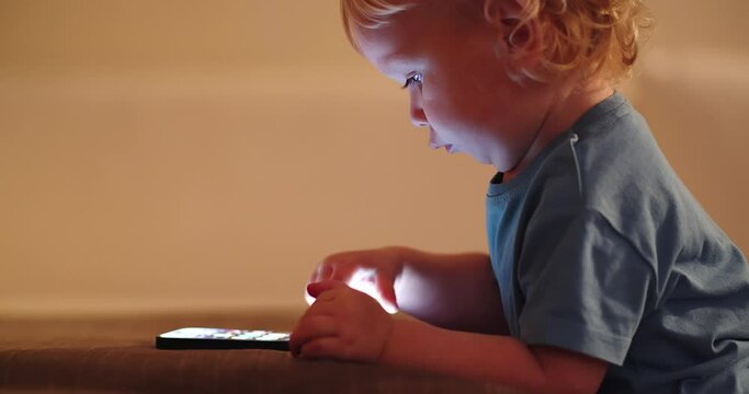 Small Baby pressing and  scrolling with finger on phone touch screen.  Cute Little child learns to use new  internet technologies. Baby playing with cellphone,  at home in the evening. Real time video