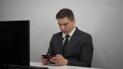 A young programmer plays a game on the phone. Businessman plays at work in the office plays smartphone.