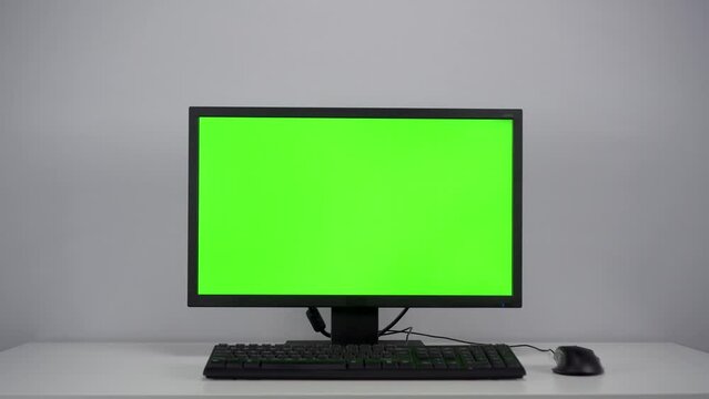 Turning on the monitor with a green screen. A man with his hand turns on the computer screen on the desktop in the office. Chroma key.