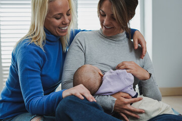 Loving female couple breastfeeding baby at home