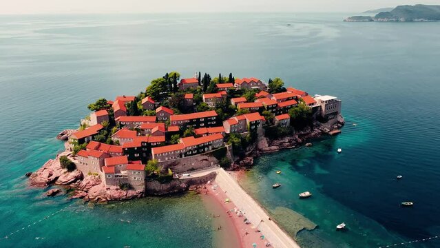 Areal shot over the picturesque little village-Sveti Stefan.Houses and buildings surrounded by the sea.4K drone shot of the beach and favourite tourist destination.Beautiful blue clear water.