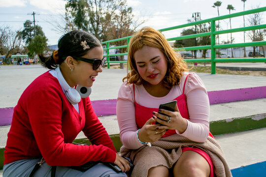 Chicas Jóvenes Viendo Videos En Teléfono Celular Sentadas En Un Parque Al Aire Libre. Mujeres Latinas