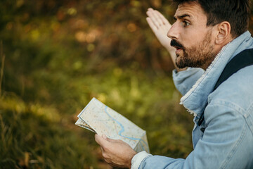 Side view of a displeased man with a map exploring the wilderness on a trekking adventure.