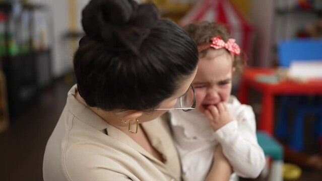 Teacher and toddler consoling girl at kindergarten