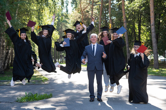 A university professor and seven robed graduates are jumping outdoors.
