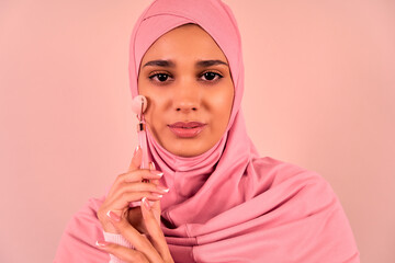   A beautiful, young, modern Muslim woman uses a massage quartz roller for her face. Skin care.