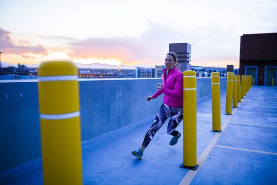Full length of determined sportswoman running through bollards on terrace during sunset