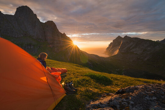 Female hiker watches sunset over Bunes beach from outside tent