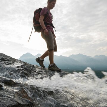 Young man hikes down ridge past mtn stream