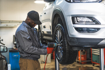 Mechanic changing tyres using an electric wrench car is lifted for a smooth process. High-quality photo