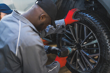 A mechanic replacing car wheels using an electric wrench tyre mounting equipment. High-quality photo