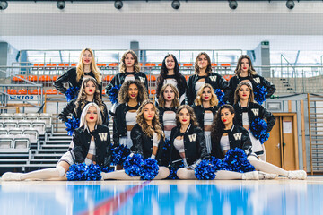 Front shot of a group of cheerleaders posing in their uniforms and blue pom-poms. High quality photo