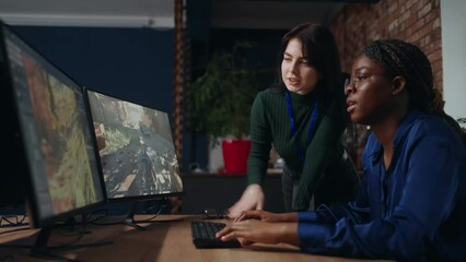 two female game designers discussing draft in office, black and caucasian ladies are looking at display