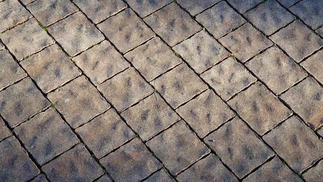 Stone tiles pavement made of granite or marble - pattern of brown floor paving as background. Texture of rough wavy uneven surface revealed by side lighting.