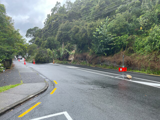 View down a road shows a land slip with trees and mud blocking a road after heavy rainfall in New Zealand.Warning signs.National emergency.Climate change