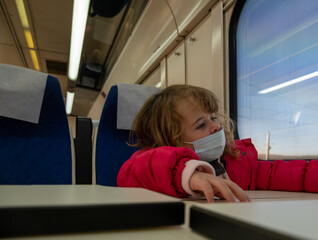 Small girl wearing mask bored in train carriage