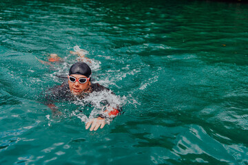 A triathlete in a professional swimming suit trains on the river while preparing for Olympic...