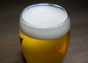 A glass of light beer with thick white beer foam    