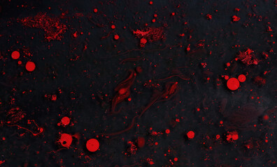 Bright red paint splashes on a thinner solution forming an abstract pattern. Selective focus on black background.