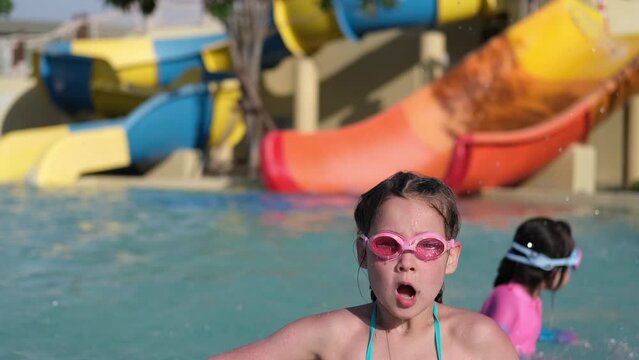 Close-up video of a little girl in a purple swimsuit standing in the pool and wearing swimming glasses. happy kid having fun in the water, beach resort, summer vacation and holiday concept.