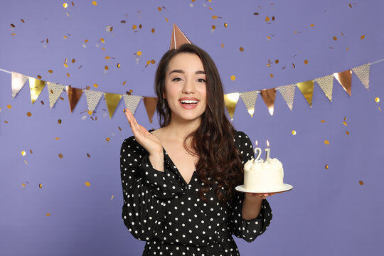 Coming of age party - 21st birthday. Smiling woman holding delicious cake with number shaped candles on violet background