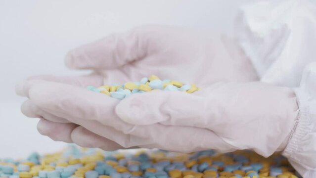 hands in latex gloves pour multi-colored pills from palm to palm on a bedlam background Medicine Pharmacy Health