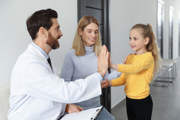 Fototapeta premium Happy mother and daughter having appointment with doctor. Pediatrician and patient giving high five in clinic